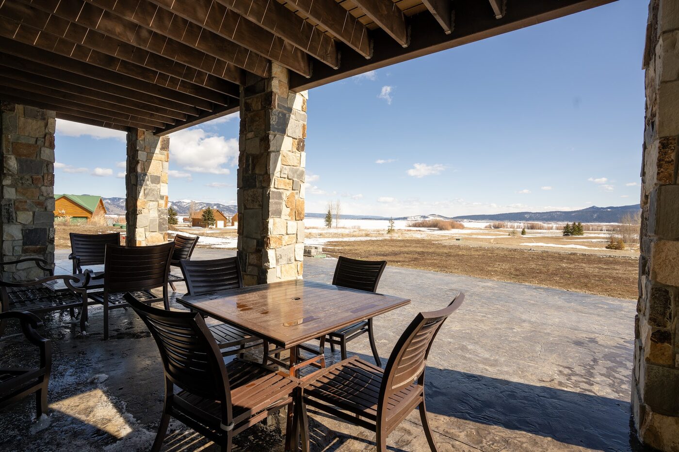 Beautiful Views — covered porch with outdoor dining table looking out at Henry's Lake and snow