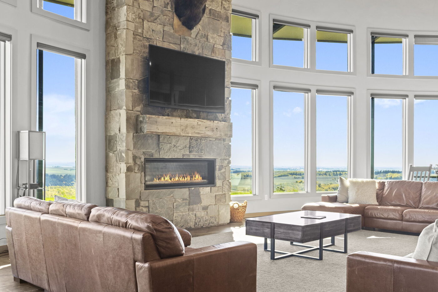 Teton View Retreat — West Cabin — great room with two-story stone fireplace and wall of windows facing the Tetons