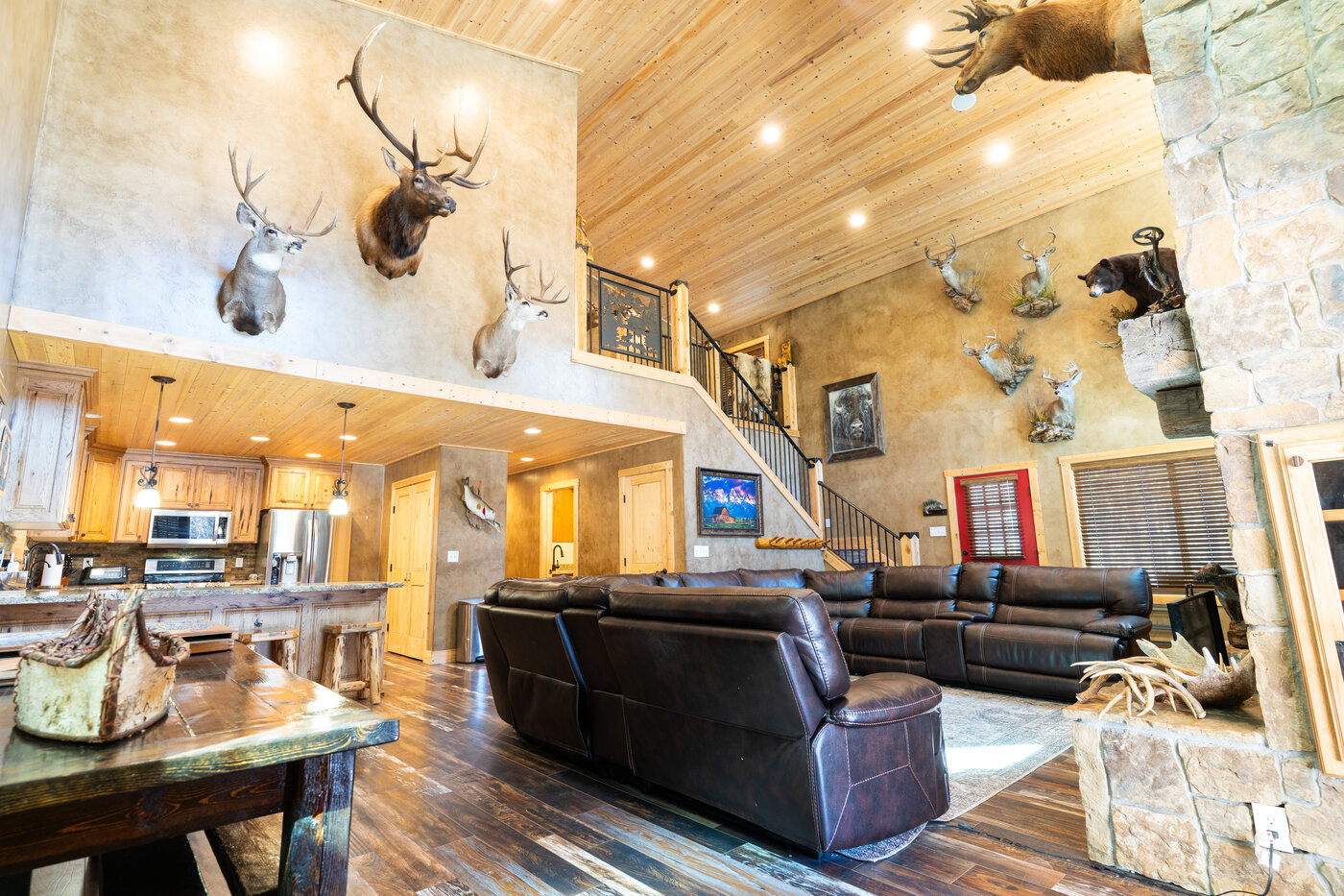 Trails End Lodge — great room with massive taxidermy gallery, leather sectional, and bear over stone fireplace
