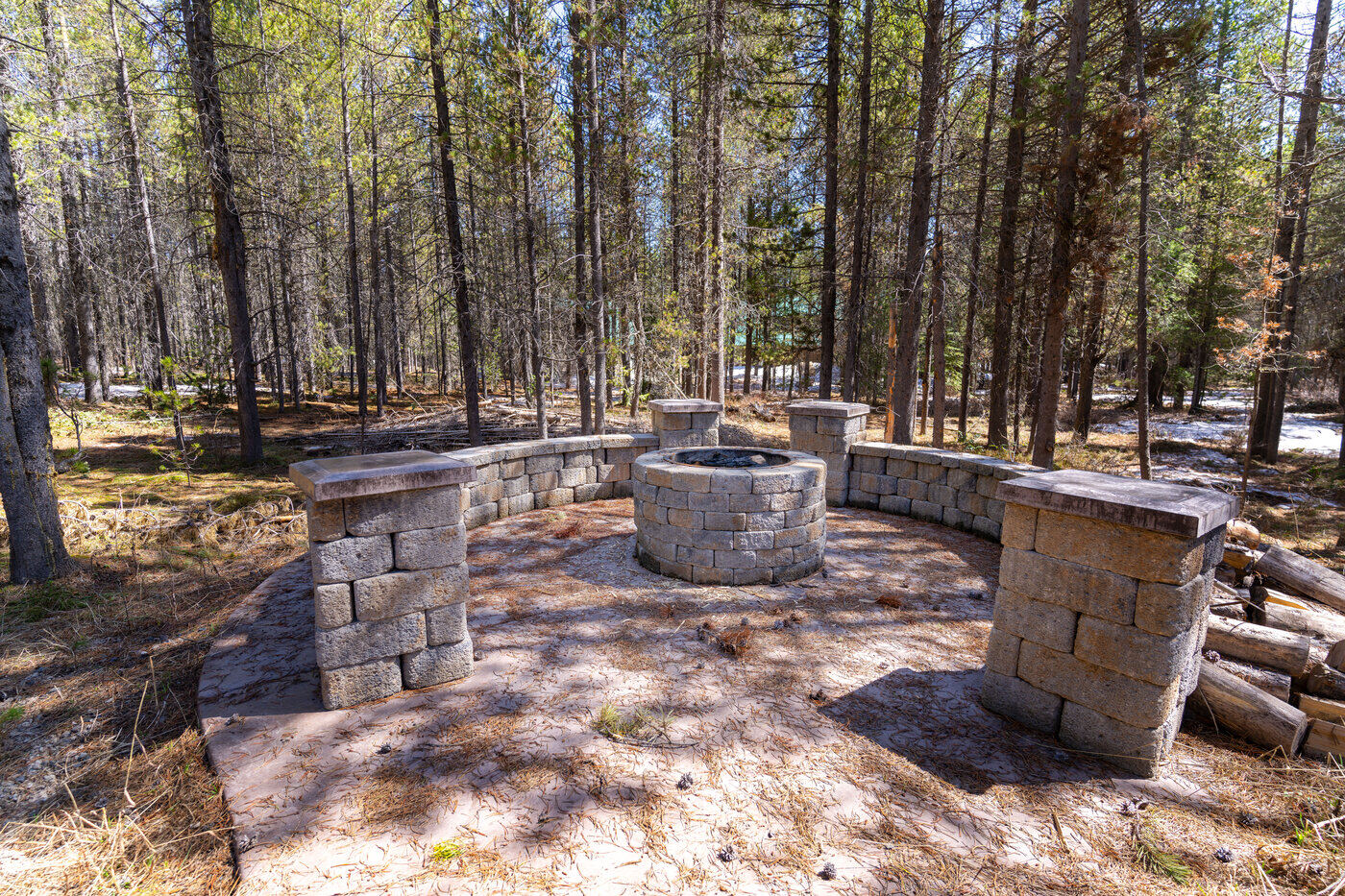 Trails End Lodge — outdoor stone fire pit ringed with built-in stone benches in the pine forest